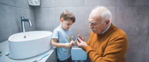 Isoisä auttaa poikaa hampaiden harjauksessa.